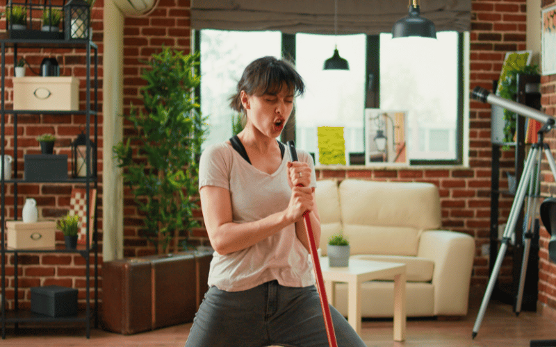 Jovem mulher animada enquanto varre a casa para ilustrar artigo sobre cronograma de limpeza doméstica